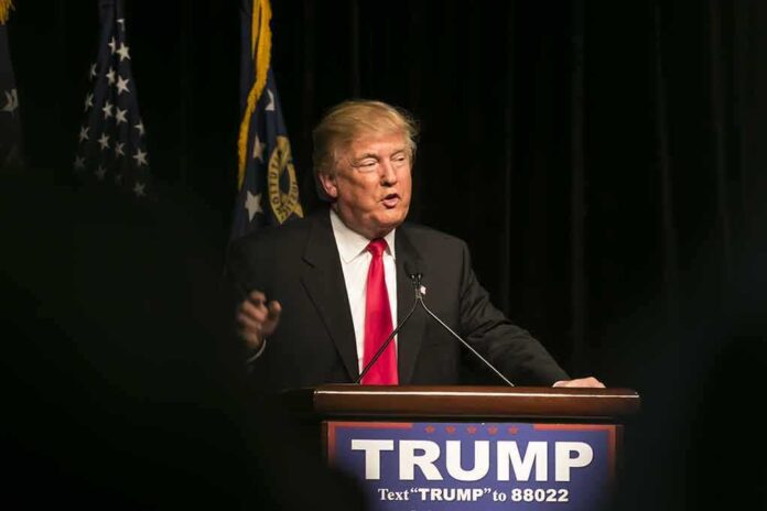 403318090 featured image Man speaking at podium with "TRUMP" sign.