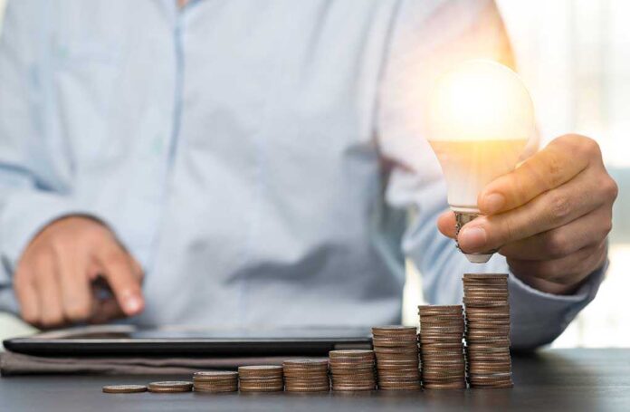 1703798617 featured image Person holding lightbulb over stacked coins