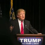 Man speaking at podium with TRUMP