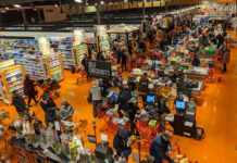 Crowded supermarket checkout area with people shopping.