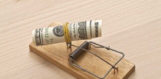 Mousetrap baited with rolled dollar bills on table