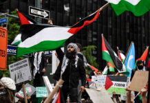 Protesters with flags and signs, one holding a megaphone