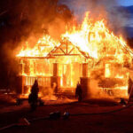 House engulfed in flames with firefighters present