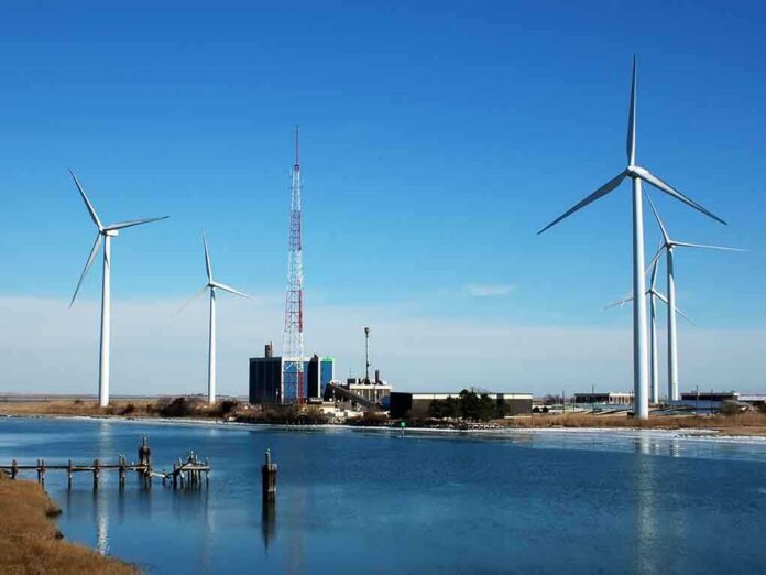 Wind turbines and a communication tower near a body of water under a clear blue sky
