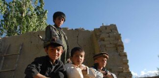 Four boys sitting and standing near a crumbling wall in a rural area