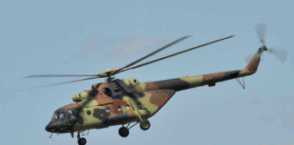 Camouflage military helicopter in flight against blue sky.