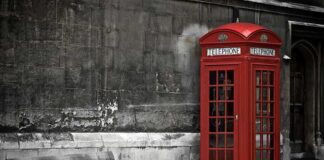 A red telephone booth next to a wooden bench against a stone wall
