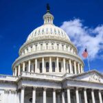 The US Capitol building with a dome and American flag against a blue sky