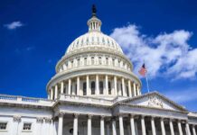 The US Capitol building with a dome and American flag against a blue sky
