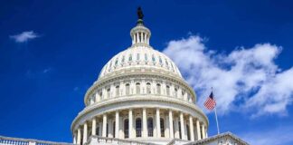 The US Capitol building with a dome and American flag against a blue sky