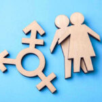 Democrat Makes ABSURD CASE For Child Transgender Surgery Wooden transgender symbol and couple figures on blue background.
