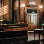 Courtroom Chaos—Murder Suspect Drops Dead Before Confession! Empty courtroom with wooden interior and green lamps.