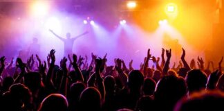Crowd at a concert with raised hands and colorful stage lights