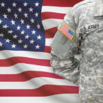 Army Deserters BUTCHER Fellow Soldier Soldier in camouflage uniform standing before American flag.
