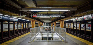 Subway station platform with directional signs overhead.