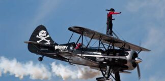 A woman performing a stunt on top of a biplane in the sky