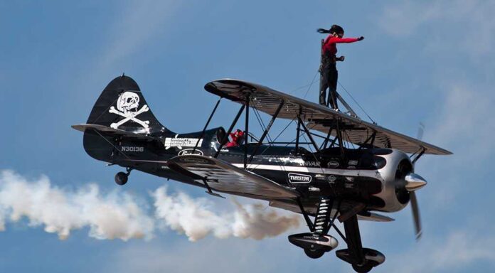 A woman performing a stunt on top of a biplane in the sky