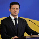 Man in suit speaking at podium with microphones.