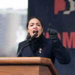 A woman passionately speaking at a podium during a rally