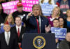 Person speaking at rally with crowd behind podium