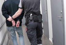 Officer escorting handcuffed person down hallway.