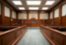 Assassins Backpack Bombshell Alters Murder Case Empty courthouse courtroom with wooden benches and chairs.