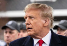 Man in suit and red tie speaking outside.