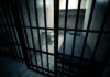 Interior view of a prison cell with a bed and metal bars
