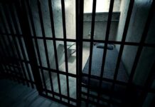 Jail Scandal: Shocking Female Officer Rape Charges Interior view of a prison cell with a bed and metal bars