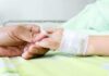 E. Coli Outbreak Across Beloved Chain – Child HOSPITALIZED! A person holding the hand of a patient with an IV in a hospital bed