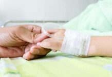 E. Coli Outbreak Across Beloved Chain – Child HOSPITALIZED! A person holding the hand of a patient with an IV in a hospital bed