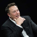 Musk Prepares Explosive Lawsuit Against Dem Rep! Man in suit smiling, resting chin on hand.