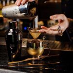 Bartender Found DISMEMBERED – Horror Couple ARRESTED! Bartender pouring a cocktail through a strainer into a gold cup