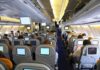 Midair Mayhem – Maniac STRANGLES Flight Attendant! Interior view of an airplane with passengers seated and using in-flight entertainment screens