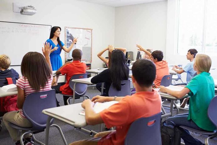 shutterstock_199144970 Teacher in a blue dress instructing students in a classroom with hands raised