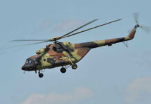 Camouflage military helicopter in flight against blue sky.