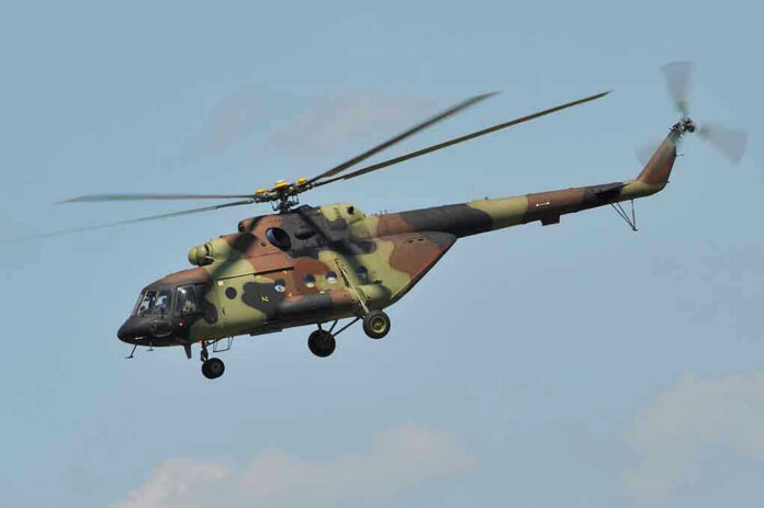 Camouflage military helicopter in flight against blue sky.