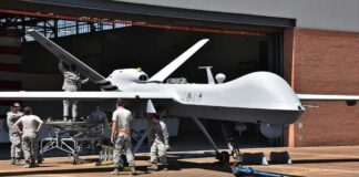 Military drone being serviced by ground crew outside a hangar