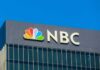 NBC Demand Reporters REMOVE This Phrase From Future Broadcasts! NBC logo displayed on a corporate building against a blue sky