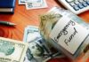 Glass jar labeled emergency fund with US dollar bills on a wooden desk