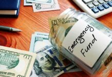 Glass jar labeled emergency fund with US dollar bills on a wooden desk