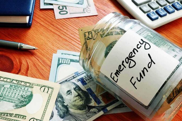 shutterstock_1695151381 Glass jar labeled emergency fund with US dollar bills on a wooden desk