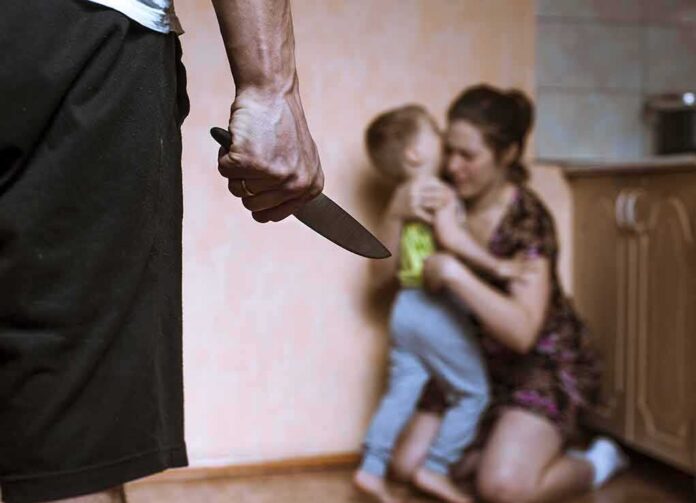 shutterstock_397265788 Man holding knife as woman shields child in kitchen