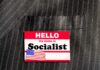 Socialist Leader Living With PARENTS in Million-Dollar House Name tag on a pinstripe suit jacket pocket
