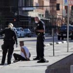 Police officers detain a seated man on a city sidewalk