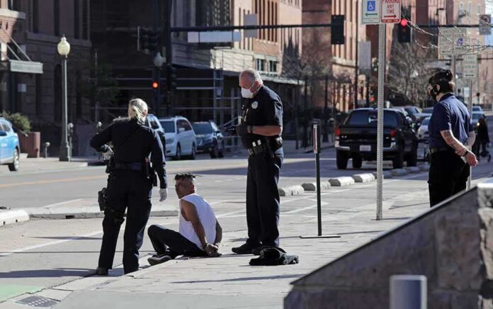 Police officers detain a seated man on a city sidewalk