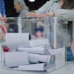 Person casting a ballot into a clear box at a polling station