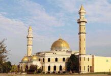 Mosque with golden dome and two tall minarets under a partly cloudy sky