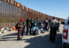Thousand Strong Migrant Caravan Headed Towards U.S Border Group of people standing by a border fence with officers and vehicles