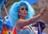 Dem Candidate’s Drag Queen OBSESSION Gets Weirder Drag performer with bright blue wig giving thumbs up at parade